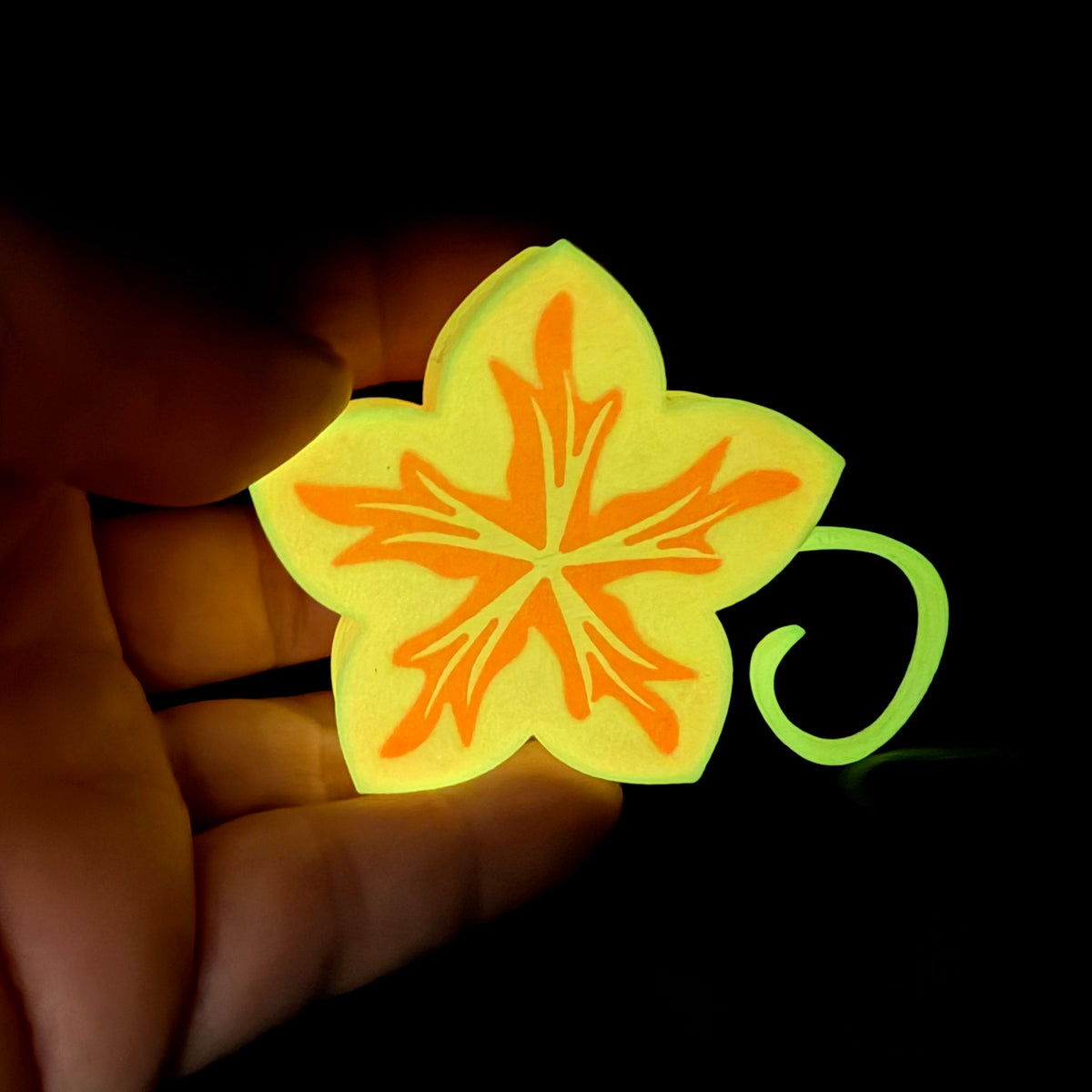 Bright yellow flower-shaped object held in a hand against a dark background